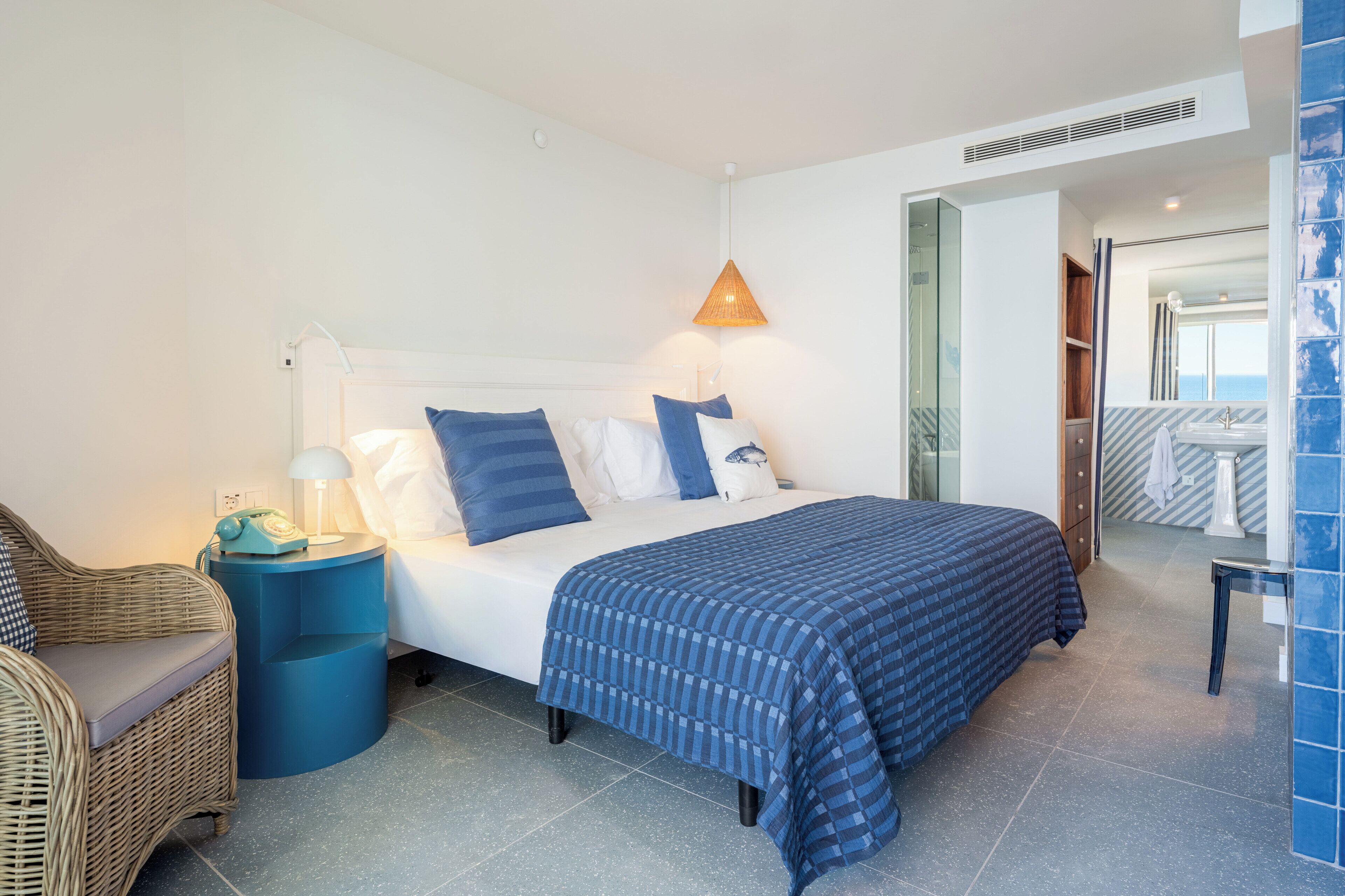 Et moderne hotelværelse med seng, stol, et natbord med lampe, og et badeværelse, der ses gennem en åben dør.