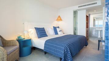 Et moderne hotelværelse med seng, stol, et natbord med lampe, og et badeværelse, der ses gennem en åben dør.