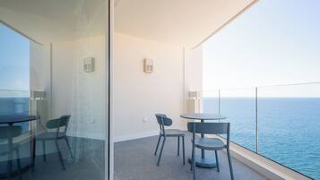 A balcony with a glass partition, a round table, two chairs, and a view of the sea.