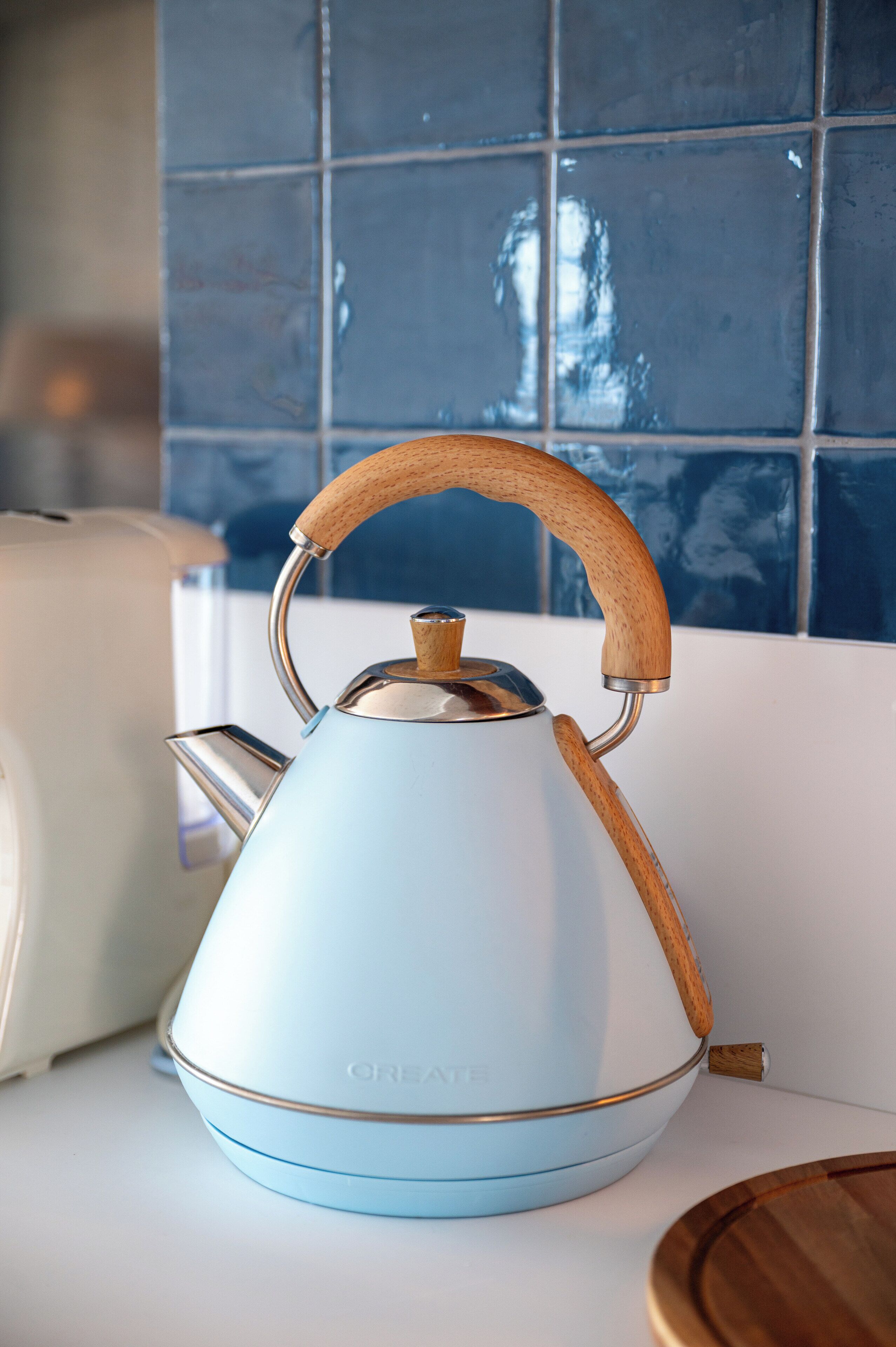A light blue kettle with a wooden handle on a white countertop.