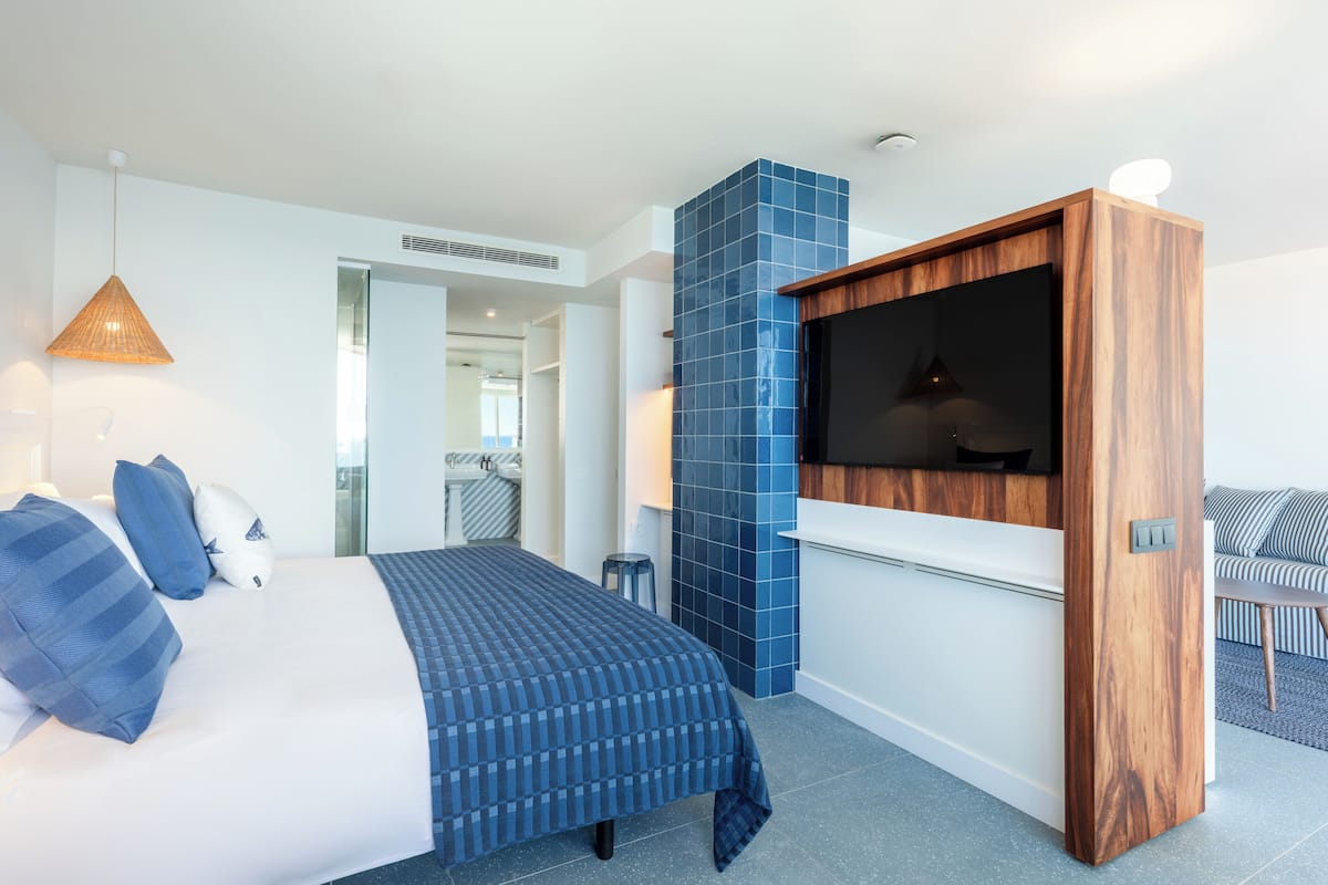 A modern hotel room with a bed, a TV, and a blue-tiled wall.