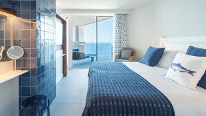 A hotel room with a bed, a chair, a small table, a mirror, and a view of the sea.