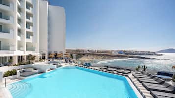 Ein Poolbereich mit Liegestühlen und Blick auf das Meer.