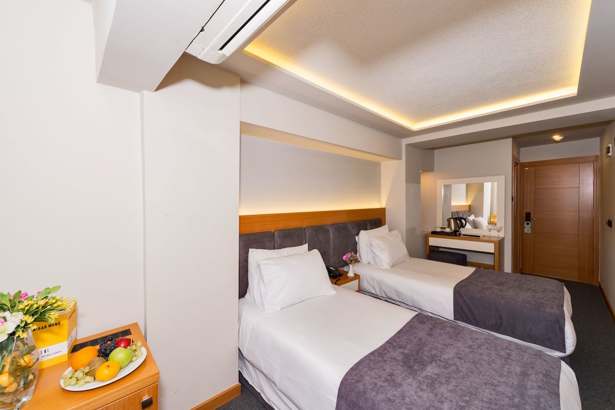 Habitación de hotel con dos camas, un escritorio y una pequeña mesa con frutas y flores.