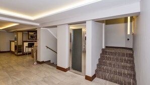 A spacious hallway with a carpeted staircase, a door with a metal gate, and a bar area in the background. - Bergama Hotel (Istanbul)