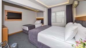 A hotel room with a large bed, a smaller bed, a TV mounted on the wall, a desk, and a trash bin. - Bergama Hotel (Istanbul)