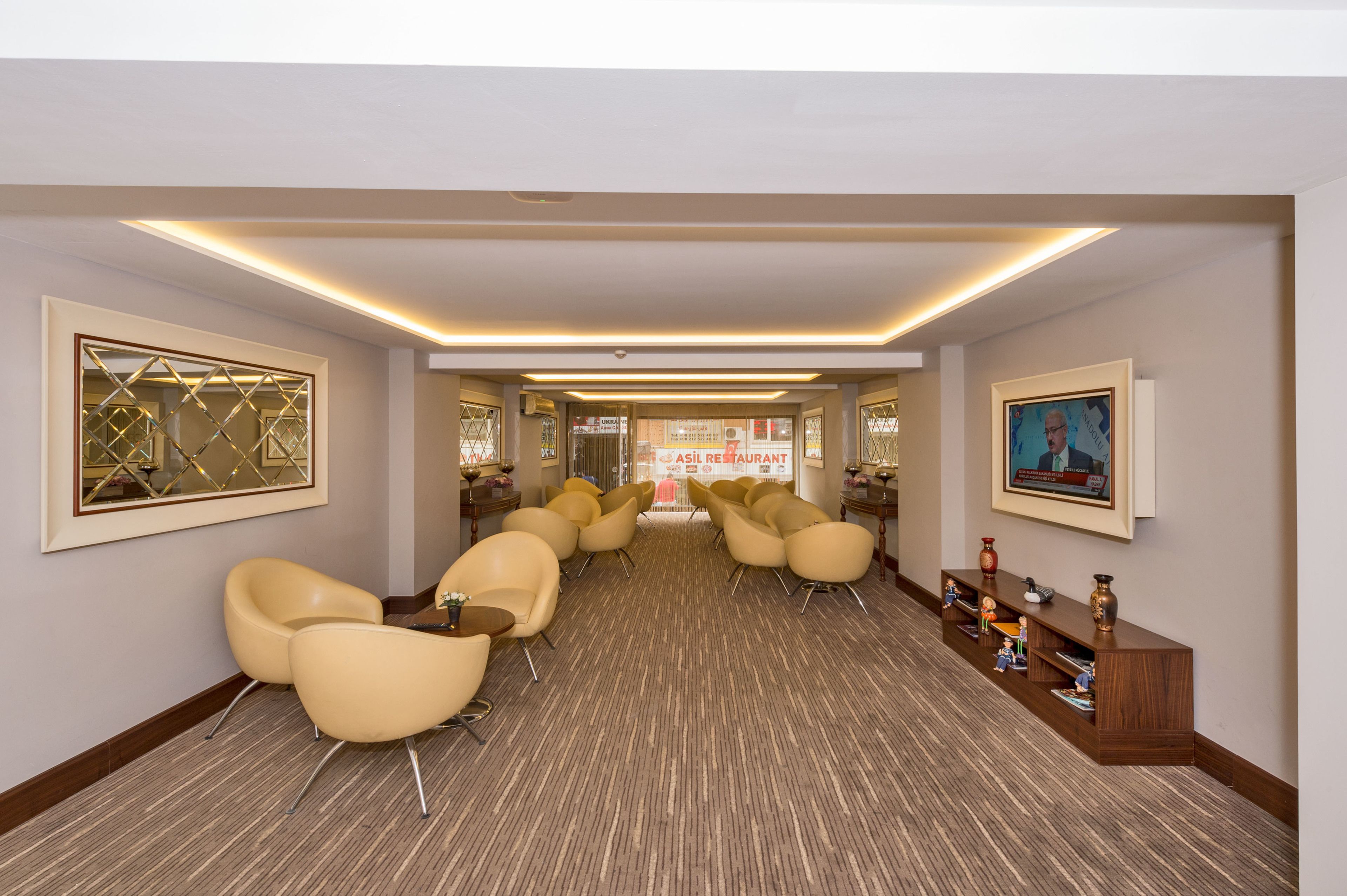A hotel lobby with a long reception desk, multiple seating areas with chairs, and framed artwork on the walls.