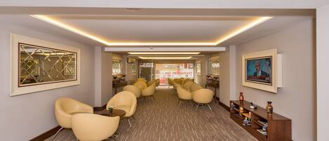 A hotel lobby with a long reception desk, multiple seating areas with chairs, and framed artwork on the walls.