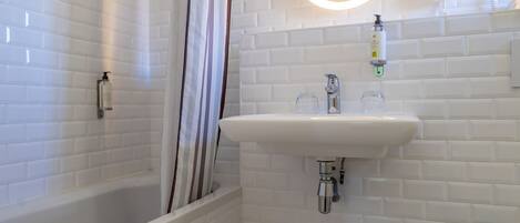 A modern bathroom with a white tiled shower, a sink with a round mirror, and a handheld showerhead.
