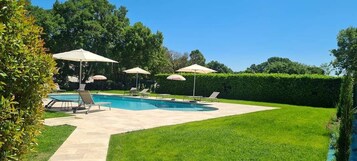 A backyard with a swimming pool, lounge chairs, and umbrellas.