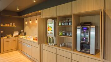 Una cocina moderna con armarios de madera, dispensador de jugo de frutas, máquina de café y panificadora.