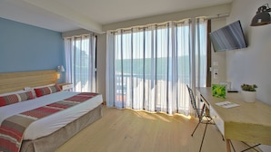 A hotel room with a bed, a desk with a chair, a TV, and a balcony with curtains. - Le Belvedere (Rocamadour)