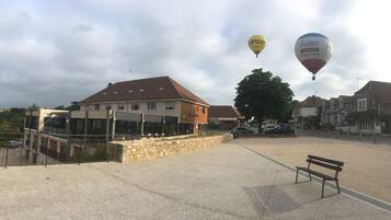 Ein Gebäude mit einer Stein-Fassade und einem roten Dach, eine Bank sowie zwei Heißluftballons am Himmel.