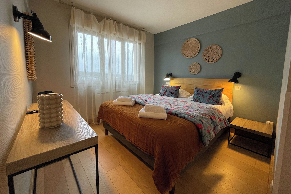 Un dormitorio con cama, mesitas de noche, una lámpara, una lámpara de pared y una ventana con cortinas.