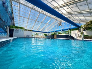 An indoor swimming pool with a glass ceiling, clear blue water, and a lifeguard warning sign. - Bolero Resort (Wildwood)