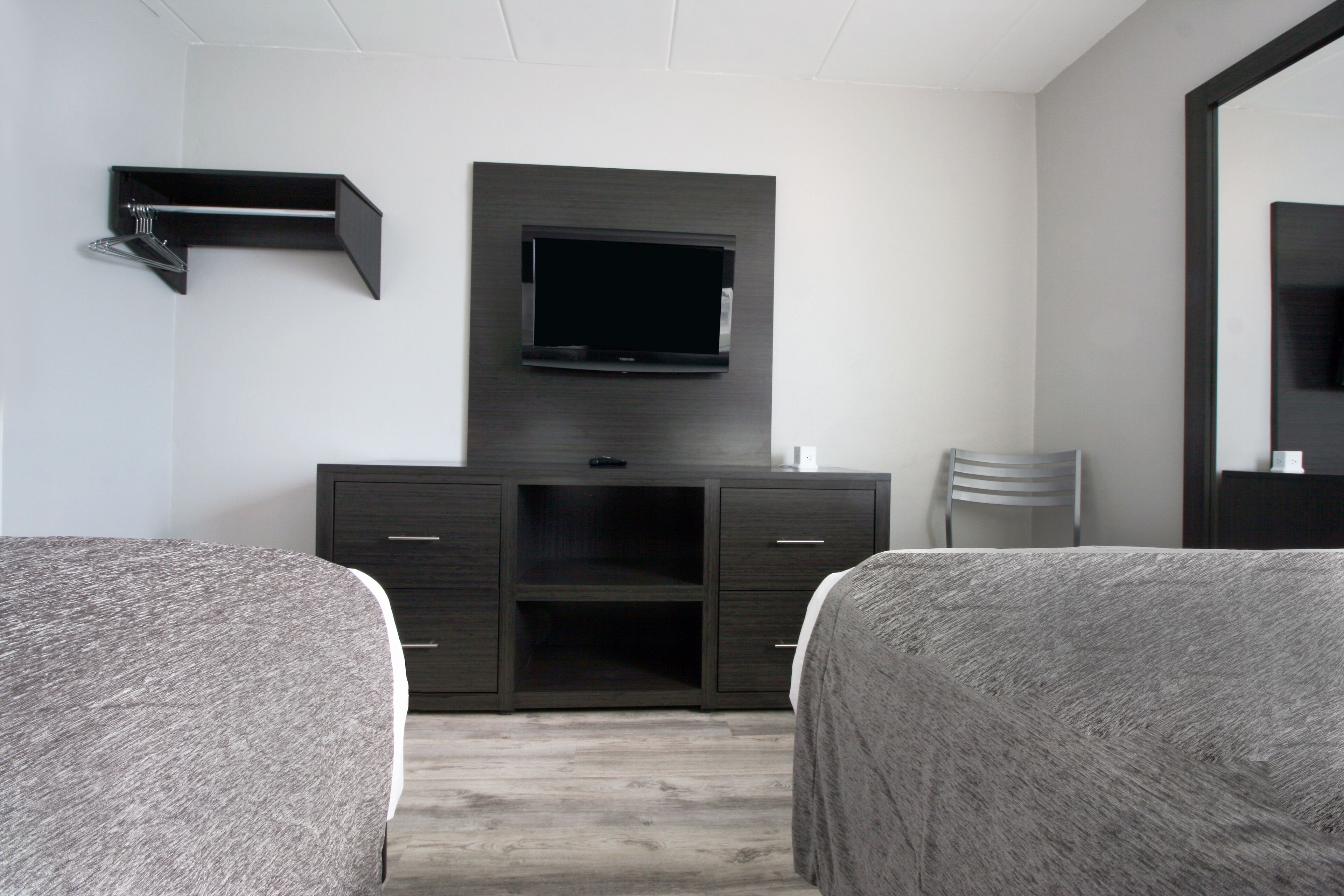 A hotel room with two single beds, a dark wooden dresser, a flat-screen TV mounted on the wall, and a mirror on the right side.