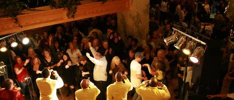 A crowded indoor event with people dancing and a stage with speakers.