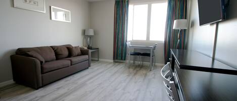 A modern living room with a brown sofa, a small table, and a TV mounted on the wall.