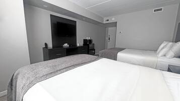 A modern hotel room with two beds, a flat-screen TV mounted on the wall, a small desk with a coffee maker, and a door with a handle.