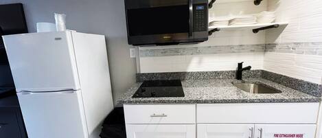 A compact kitchen with a white refrigerator, a black microwave, and a granite countertop.