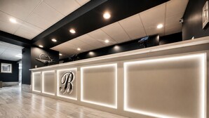 A reception desk with a large illuminated 'B' logo, recessed lighting, and a modern design. - Bolero Resort (Wildwood)