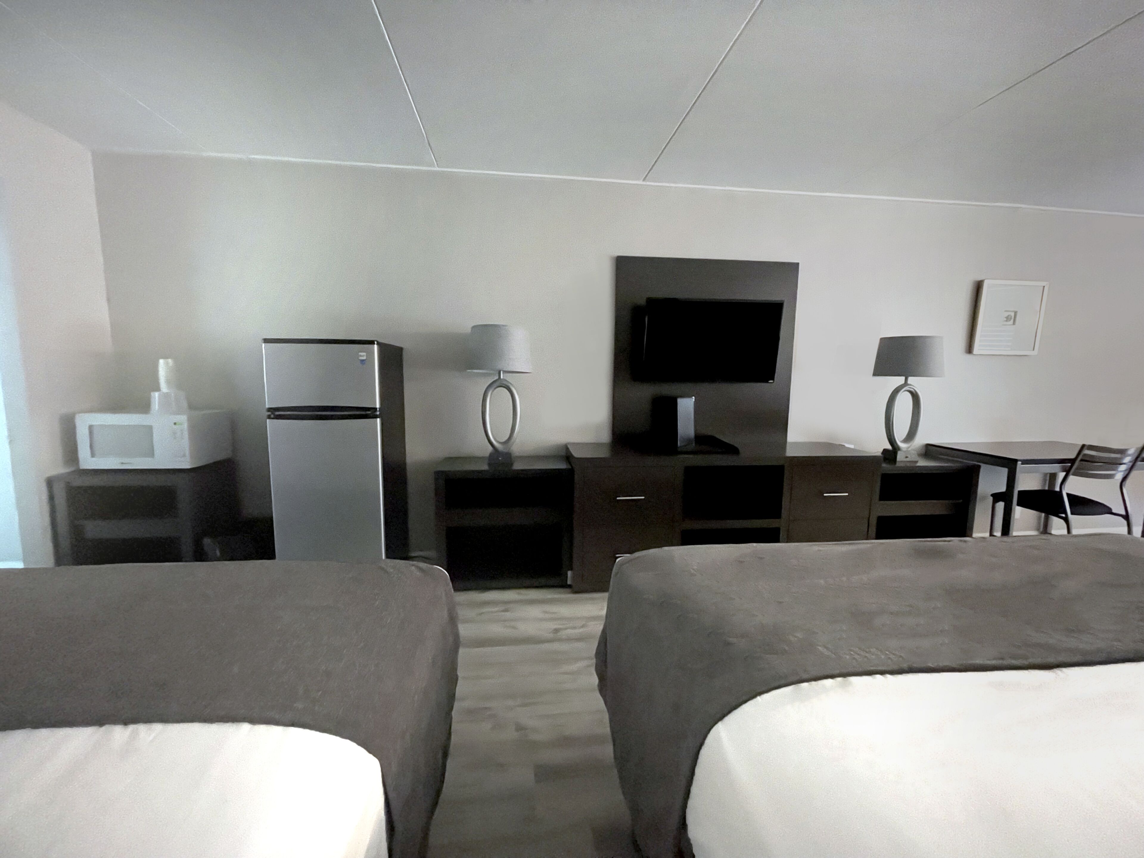 A hotel room with two beds, a refrigerator, a microwave, a flat-screen TV, a desk with a chair, and a lamp.