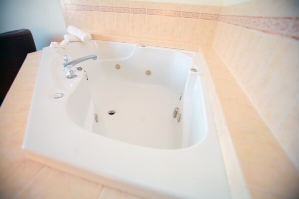 A large, empty bathtub in a bathroom with beige tiles and a decorative border.