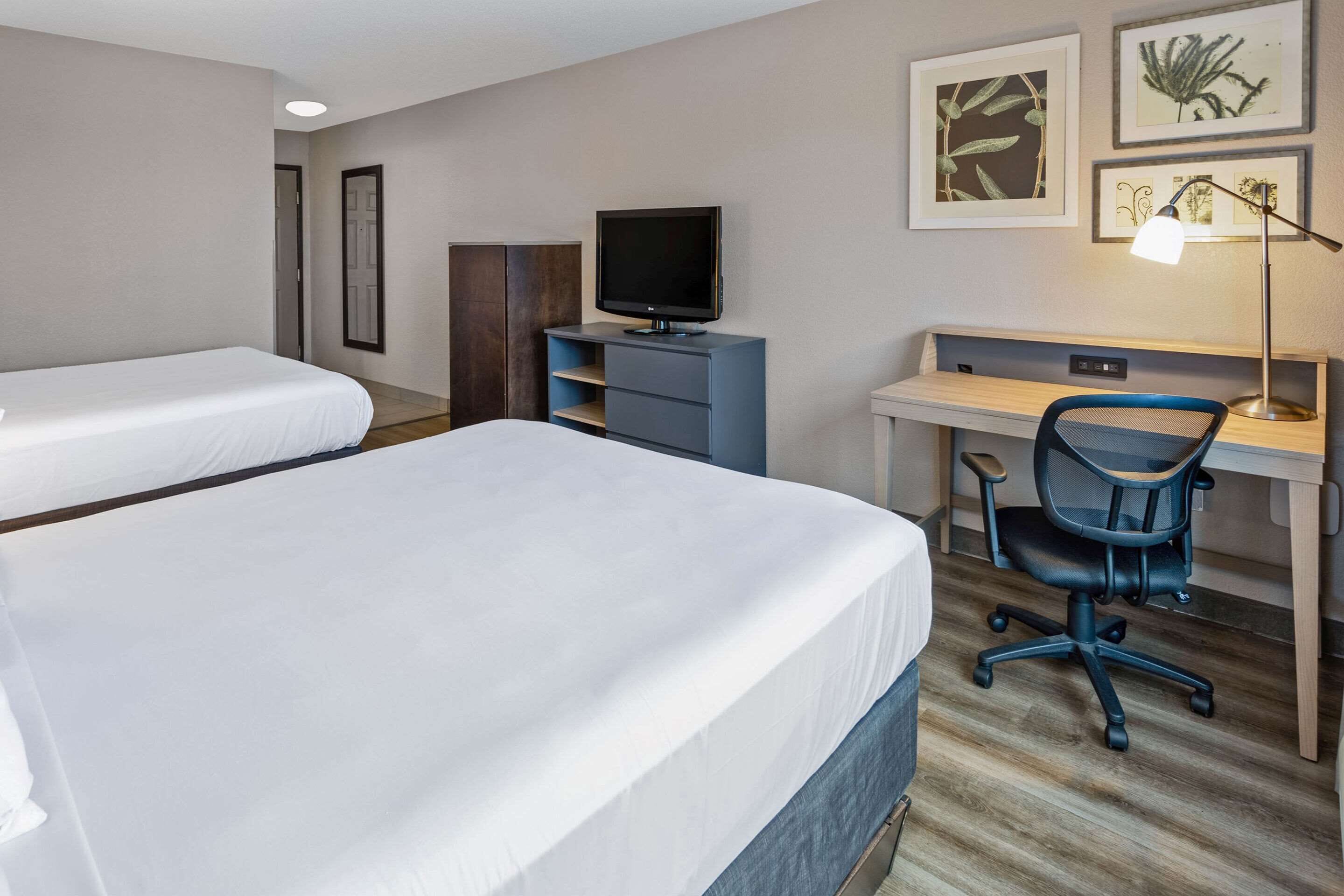 Ein Hotelzimmer mit zwei Betten, einem Schreibtisch mit Computer, einem Stuhl und einem Fernseher.
