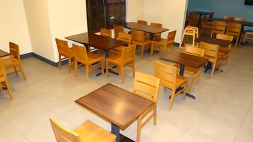 Un comedor con varias mesas y sillas de madera, dispuesto en un espacio amplio.