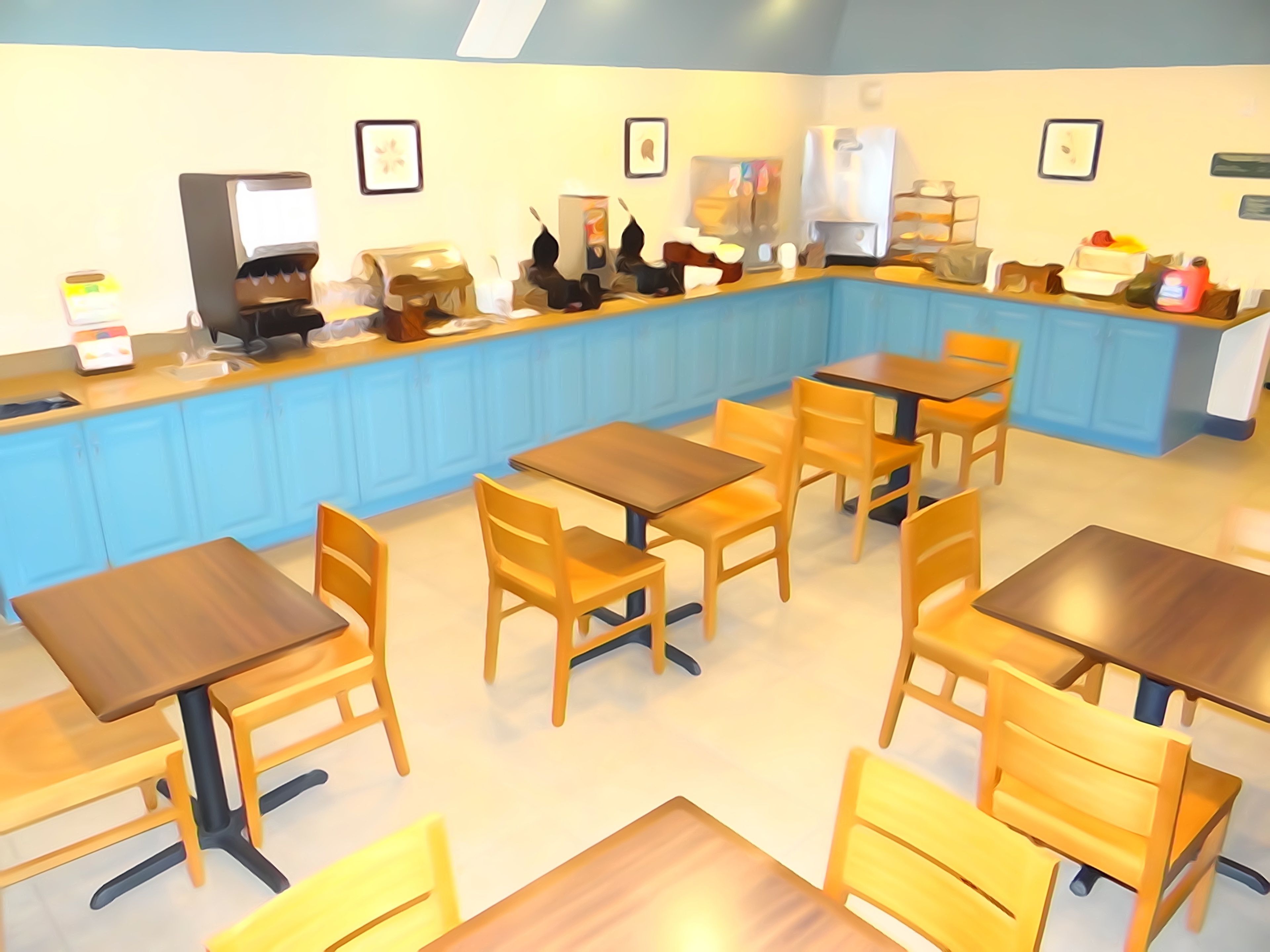 A restaurant with blue walls, wooden tables, and chairs. There are framed pictures on the walls and a coffee machine on the counter.