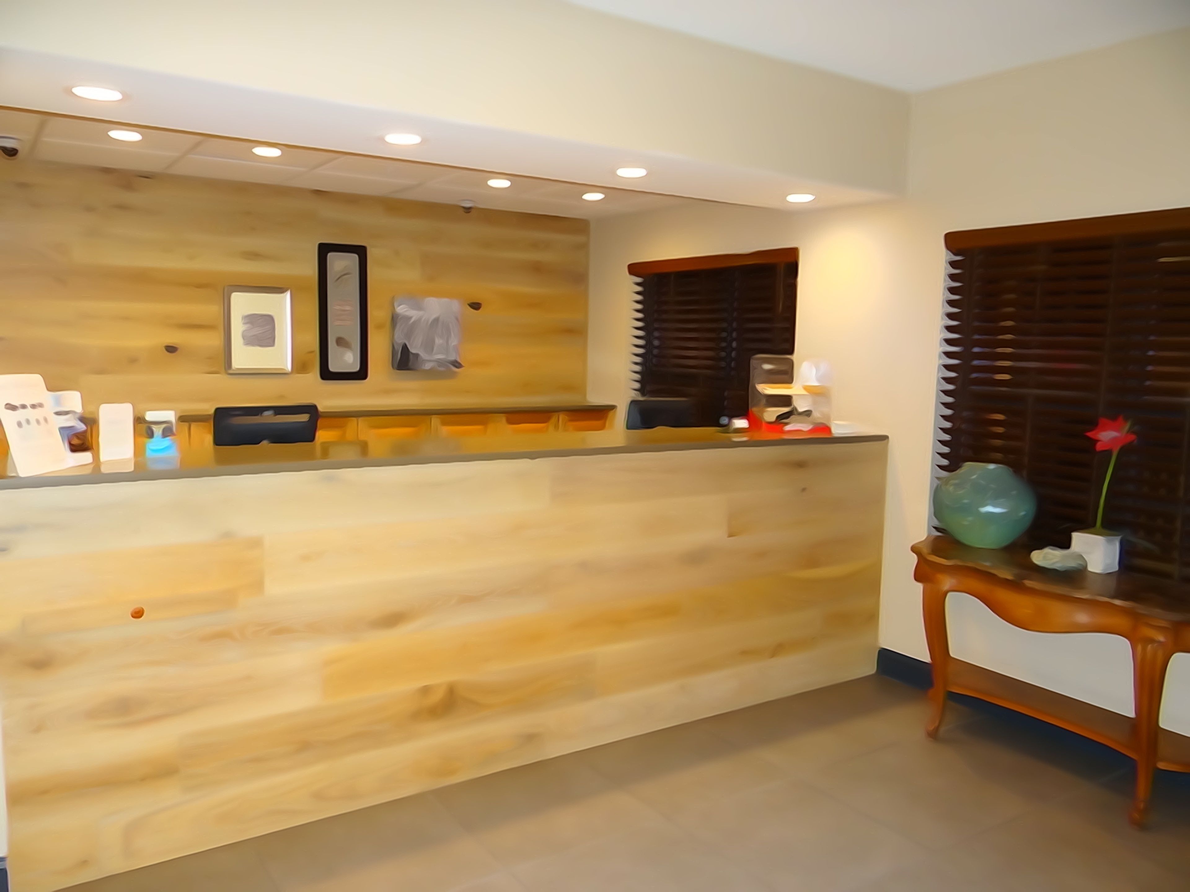 A reception desk with a wooden finish, a framed picture, and a small table with a vase and a flower.