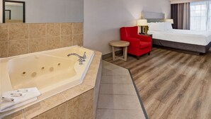 A hotel room with a large bathtub, a red chair, a small round table, and a bed with white linens. - Country Inn & Suites by Radisson, Salisbury, MD (Salisbury)