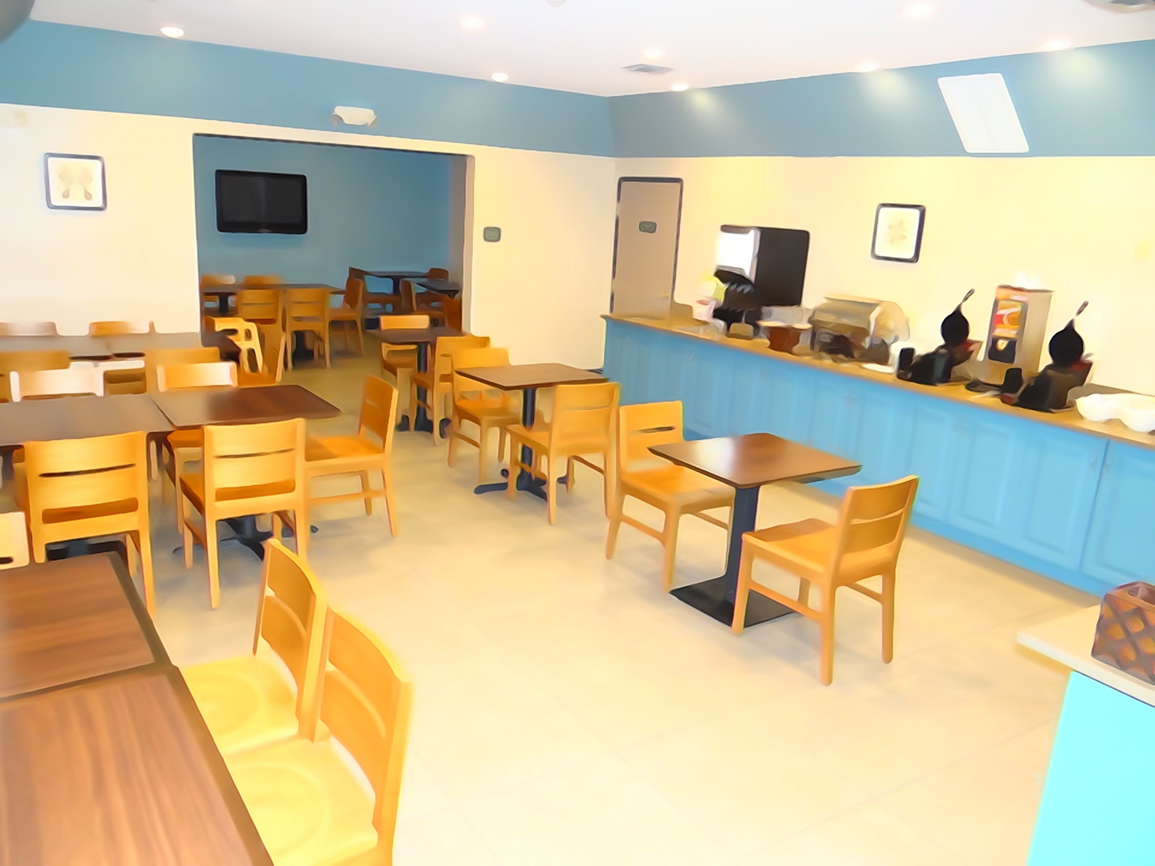 Un restaurante con mesas y sillas de madera, una barra azul con una caja registradora y un televisor colgado en la pared.