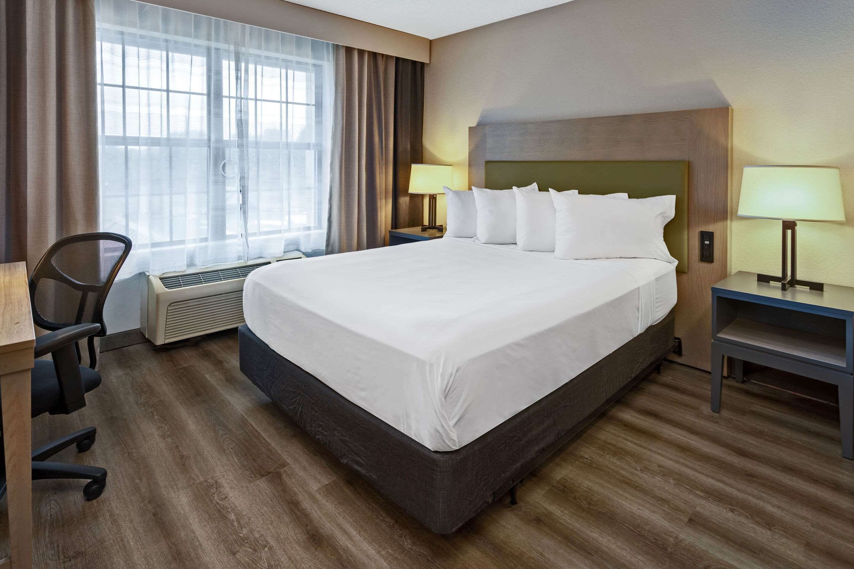 A hotel room with a large bed, two bedside tables with lamps, a chair, a desk, and a window with curtains.