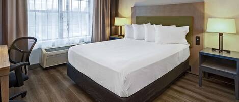 A hotel room with a large bed, two bedside tables with lamps, a chair, a desk, and a window with curtains.