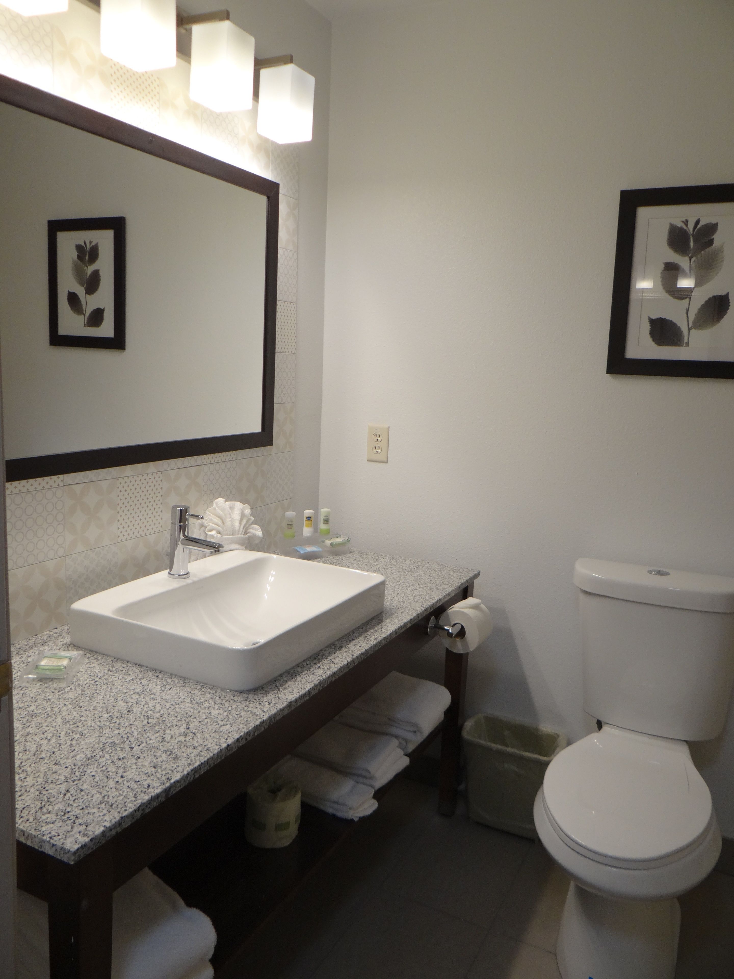 A bathroom with a white sink, a mirror, and a toilet. There are towels and toiletries on the counter.