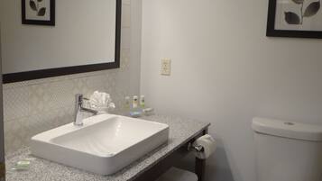 A bathroom with a white sink, a mirror, and a toilet. There are towels and toiletries on the counter.