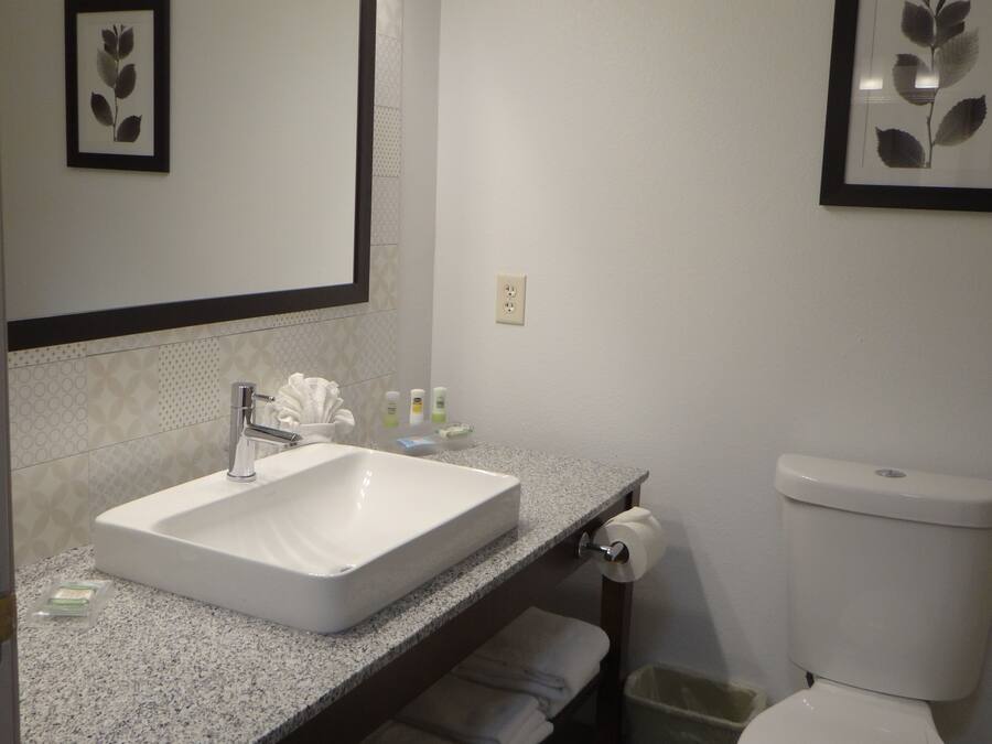 A bathroom with a white sink, a mirror, and a toilet. There are towels and toiletries on the counter.
