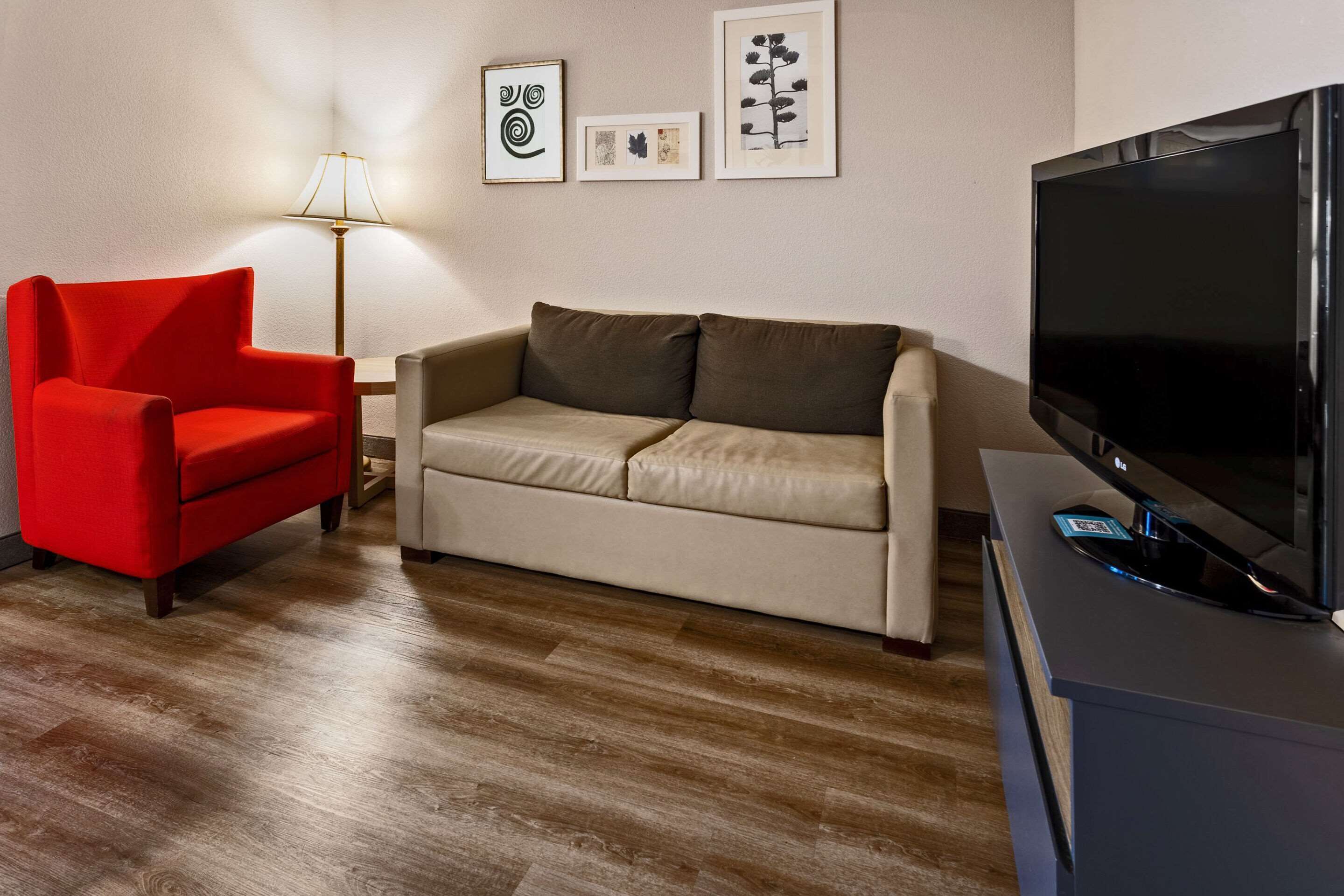 Una sala de estar con un sillón rojo, un sofá beige, un televisor de pantalla plana y obras de arte enmarcadas en la pared.