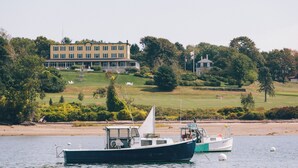A boat docked near a building with a lawn and trees in the background. - Chebeague Island Inn (Chebeague Island)