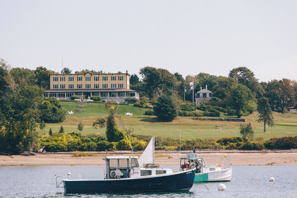 A boat docked near a building with a lawn and trees in the background.