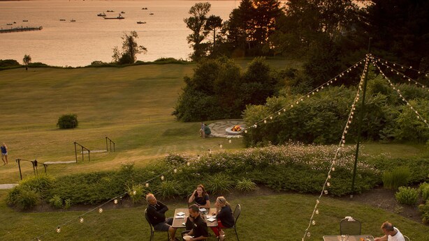 An outdoor dining area with tables and chairs, overlooking a body of water and a sunset. - Chebeague Island Inn (Chebeague Island)