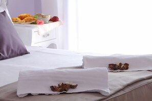 A neatly made bed with white linens and two pillows, a bedside table with a bowl of fruit and a cup, and a window with curtains. - Hotel I Due Cigni (Montepulciano)