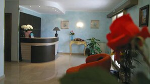A reception area with a curved desk, a lamp, and framed artwork on the wall. - Hotel I Due Cigni (Montepulciano)