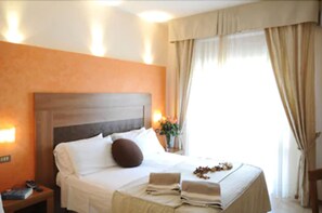 A hotel room with a large bed, a nightstand with a lamp, and a window with curtains. - Hotel I Due Cigni (Montepulciano)