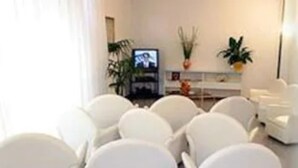 A modern living room with white furniture, a flat-screen TV, and decorative plants. - Hotel I Due Cigni (Montepulciano)