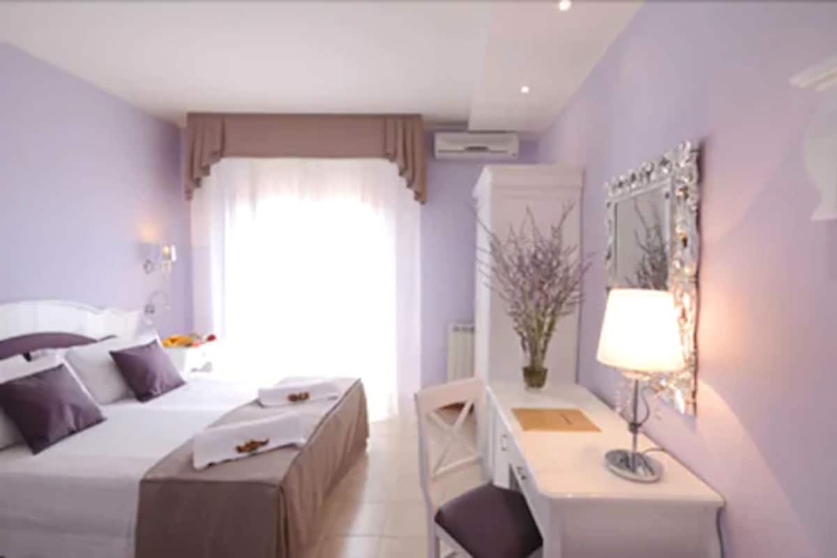 A hotel room with a bed, bedside table, chair, desk, and a mirror.