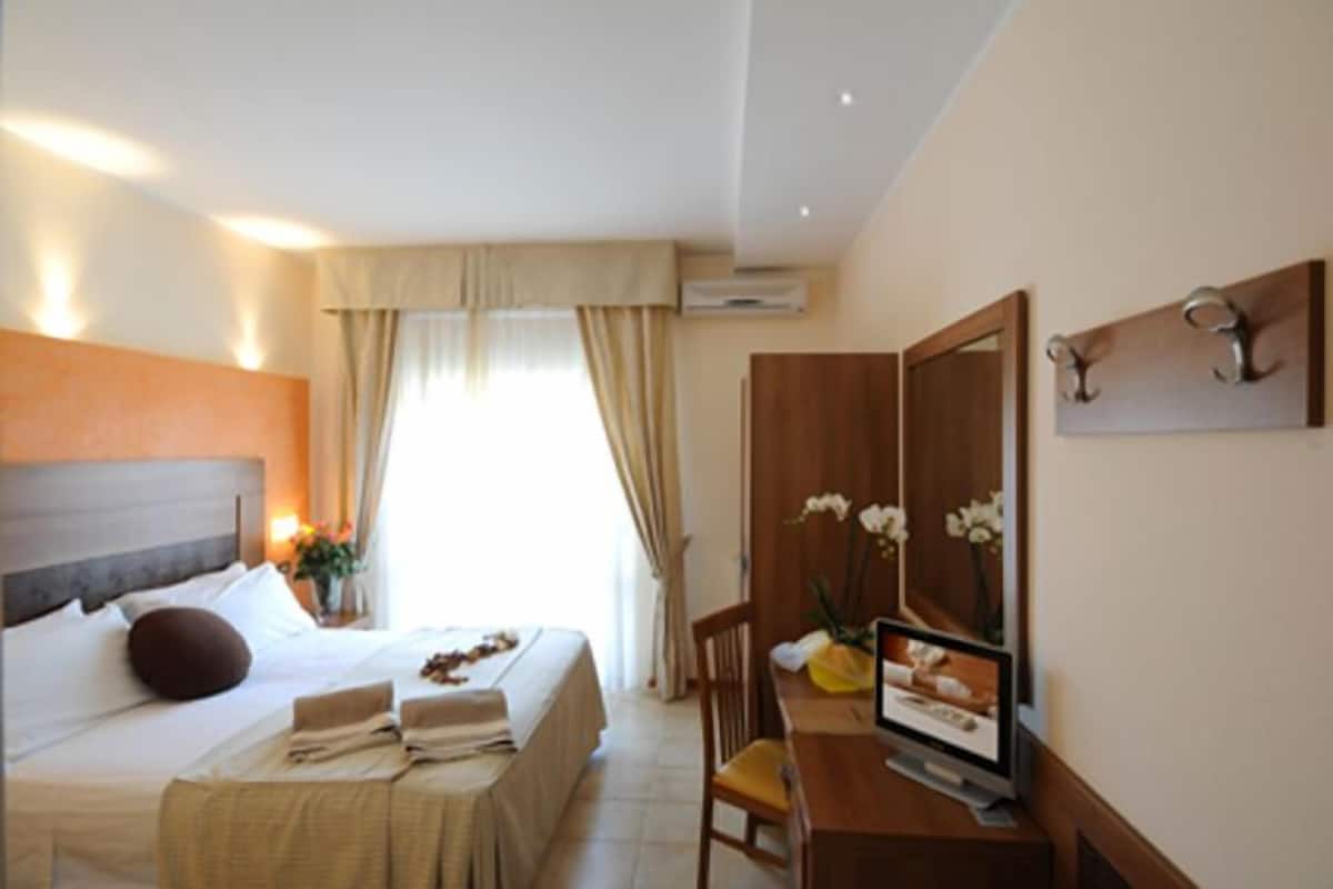 A hotel room with a bed, a desk, a chair, a TV, and a mirror.