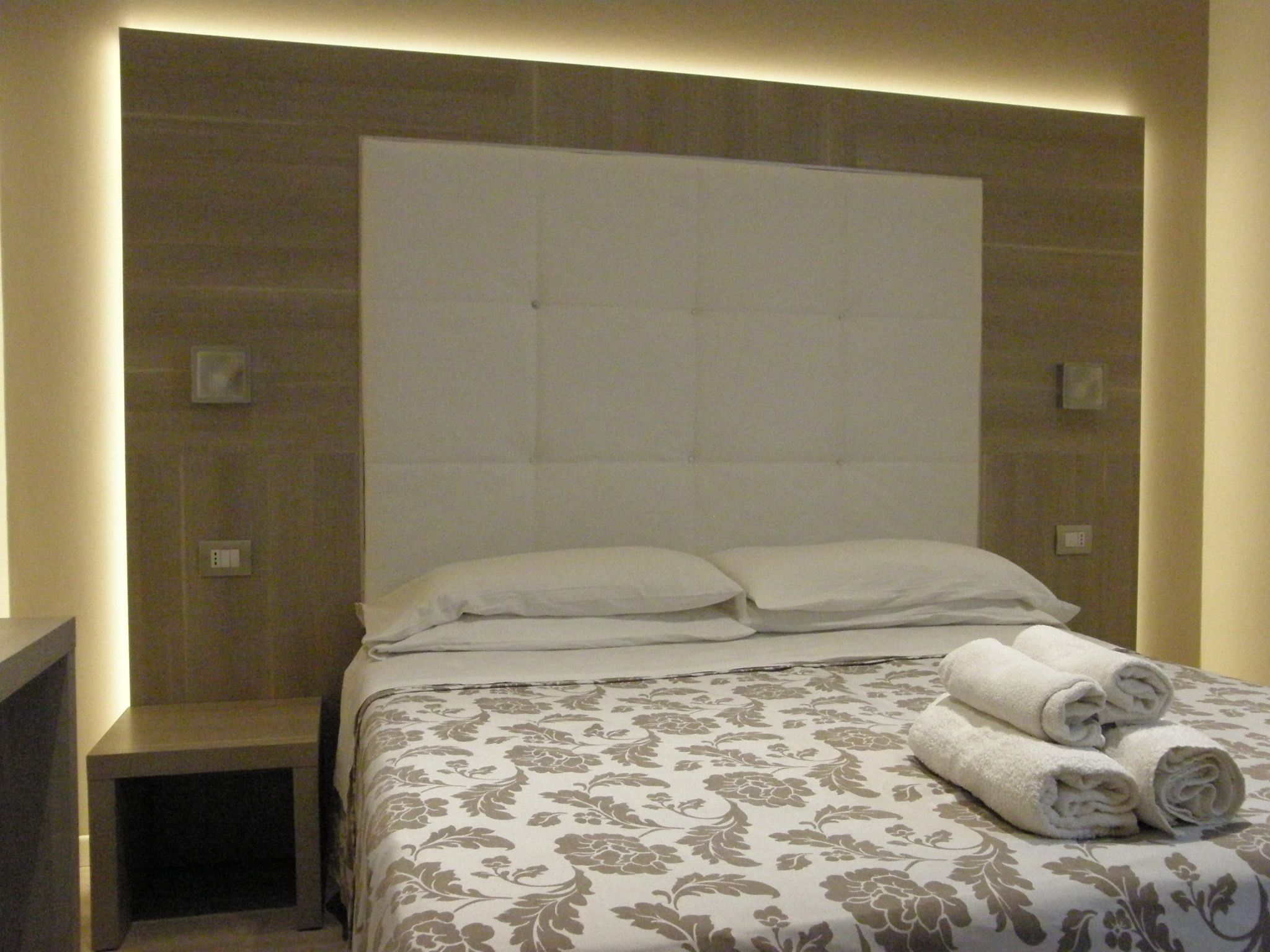 A hotel room with a large bed, a headboard, and a bedside table.