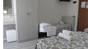 Ein Hotelzimmer mit zwei Betten, einem Kleiderschrank, einem an der Wand befestigten Fernseher und einer kleinen weißen Kommode.